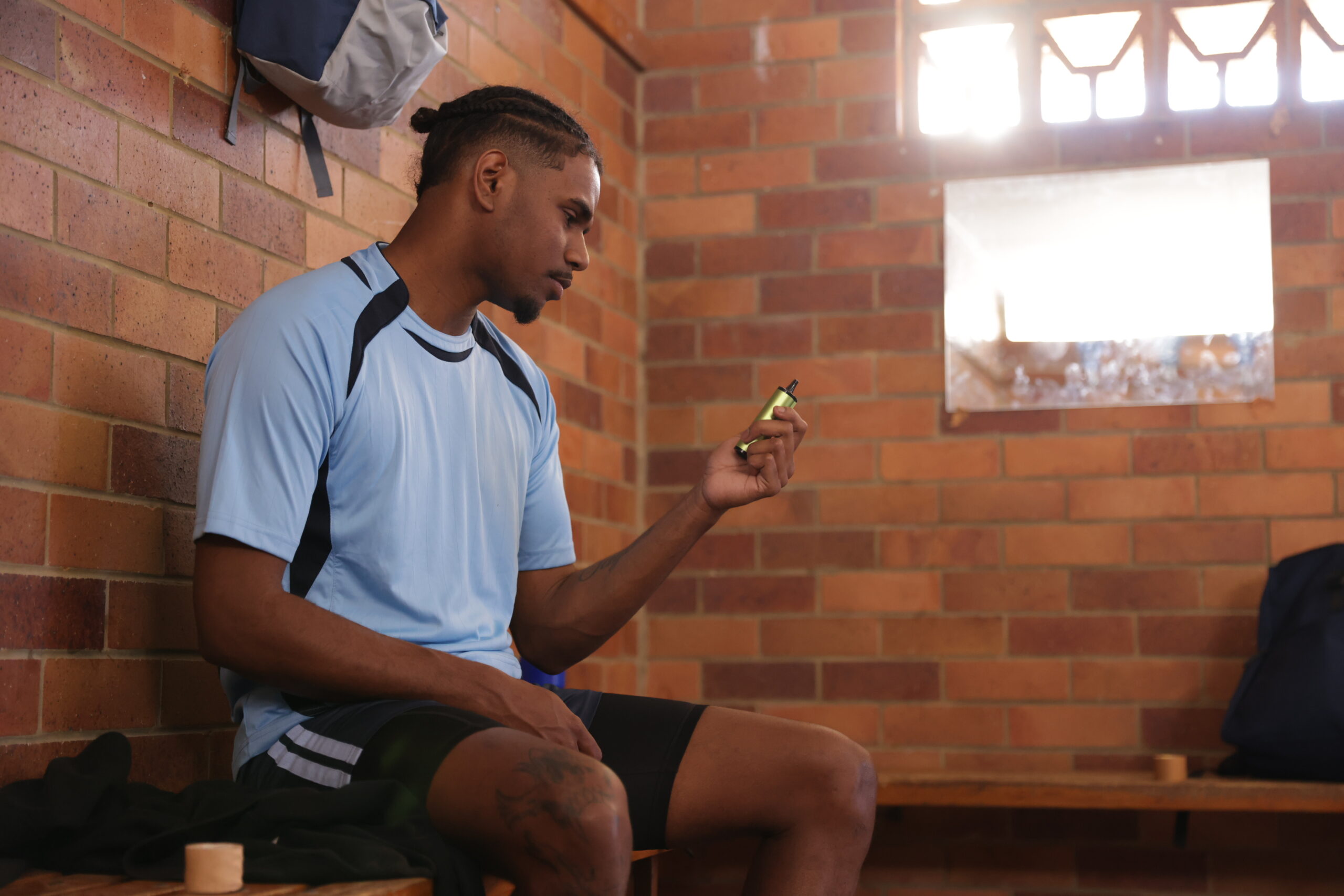 Young man in sports uniform sitting in a locker room, used for vaping information about youth and sport.
