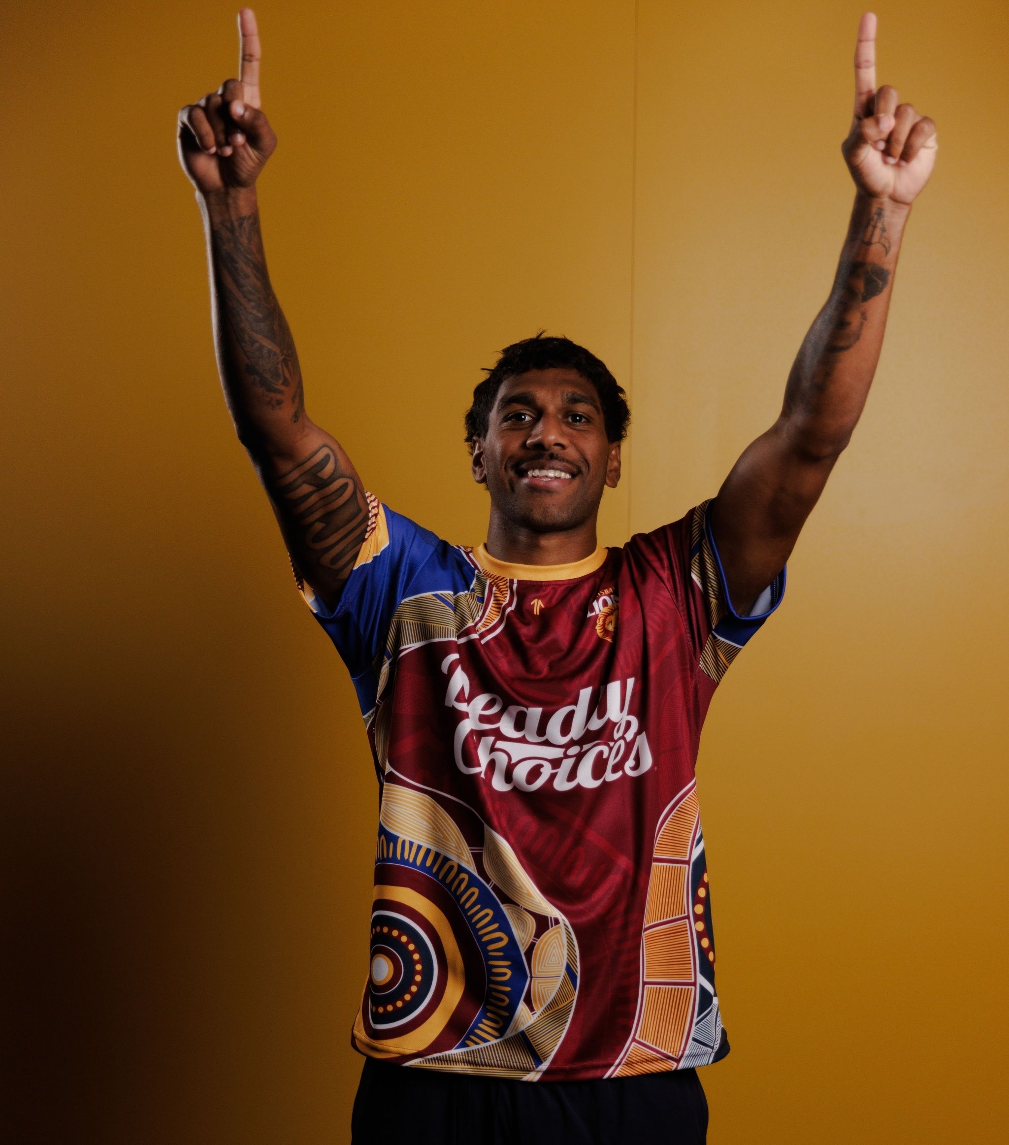 Keidean Coleman wearing a Brisbane Lions Deadly Choices Health Check shirt in 2026, pointing to the sky as he recreates a goal celebration.