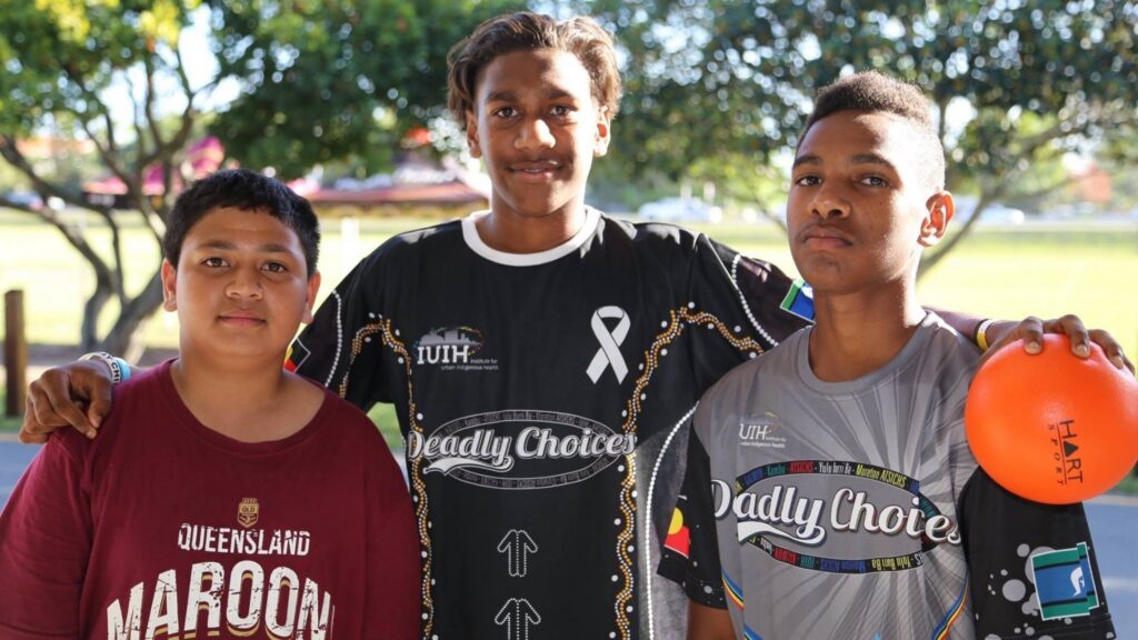 K Coleman as a child wearing a Deadly Choices shirt, holding an orange ball with his arms around two other children during the program in 2015.